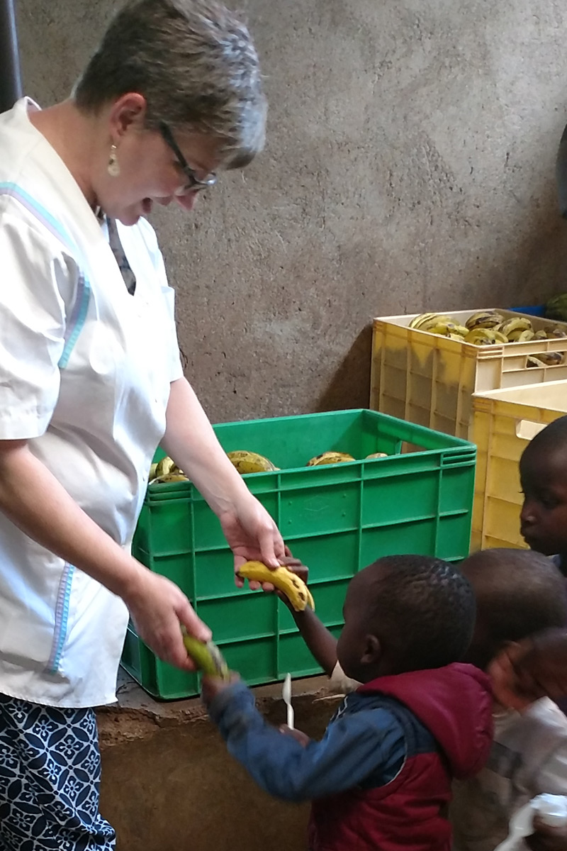 Service Learning trip chaperone Jacqueline Reich of Chestnut Hill College hands out bananas to a young boy in line at the St. Martin's feeding program in the Nairobi slums.